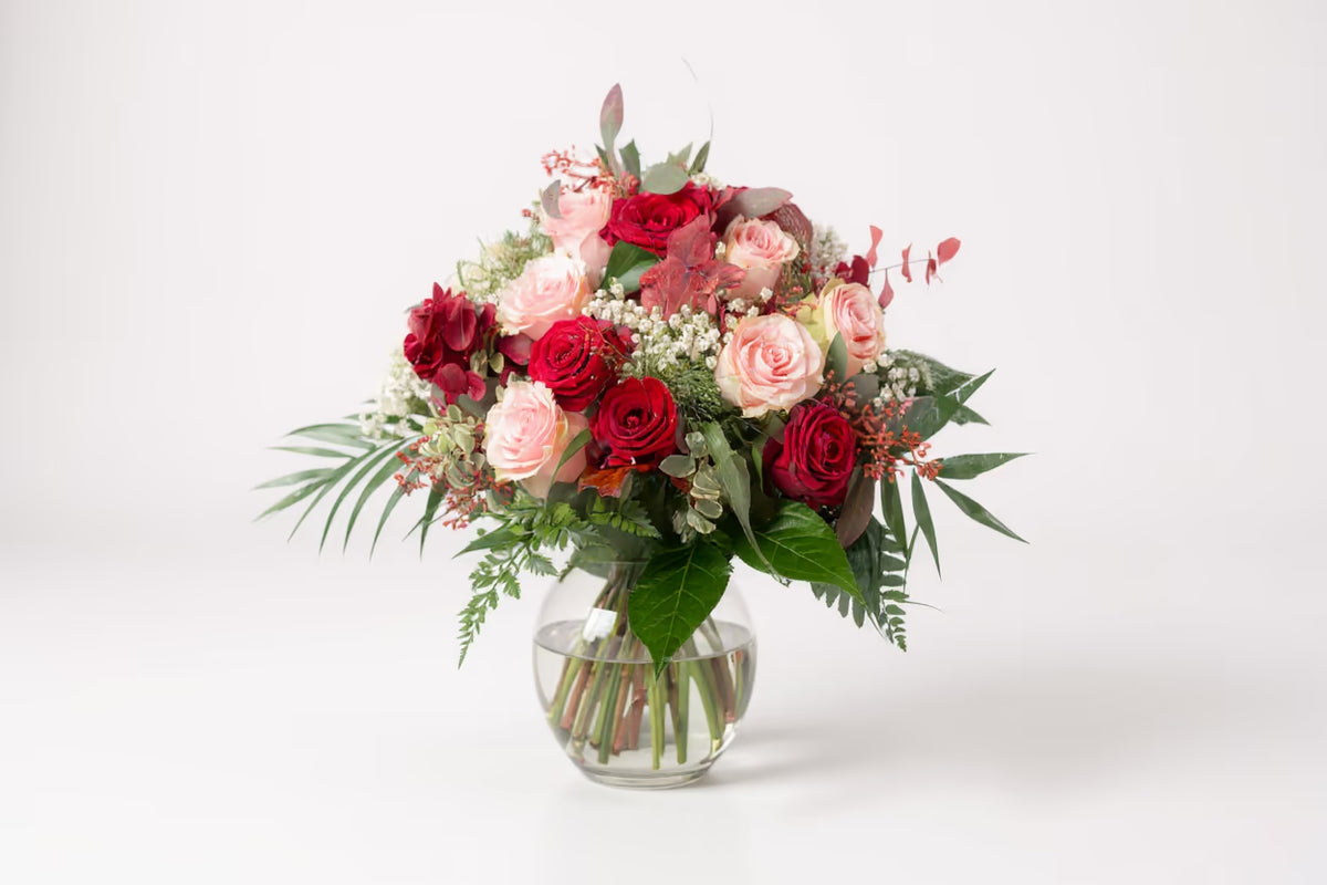 Bunter Blumenstrauß in grüner Vase vor hellem Hintergrund