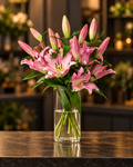 Rosa Lilienstrauß mit offenen Blüten und Knospen in einer Glasvase vor warmem FLORÉ Hintergrund